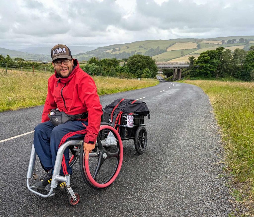 A man in a wheelchair pulling a small trailer on a road.